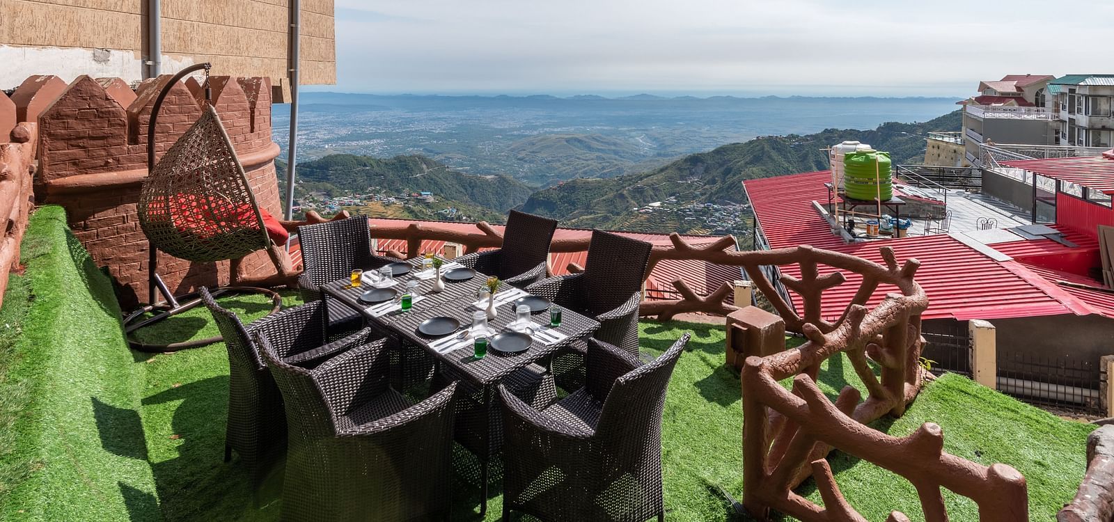 An outdoor dining area with a table and chairs set on a grassy terrace overlooking a scenic mountain landscape | DLS The Pearl
